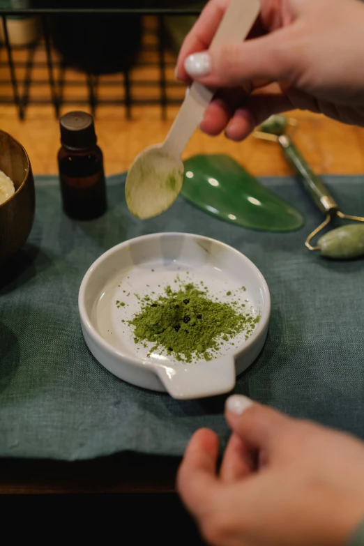 a person holding a spoon over a bowl of green tea, inspired by Kanō Shōsenin, process art, scales with magic powder, apothecary, on display, skincare