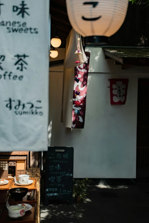 a couple of signs hanging from the side of a building, inspired by Okamoto Tarō, trending on unsplash, sōsaku hanga, celebration of coffee products, square, lush surroundings, ethnicity : japanese
