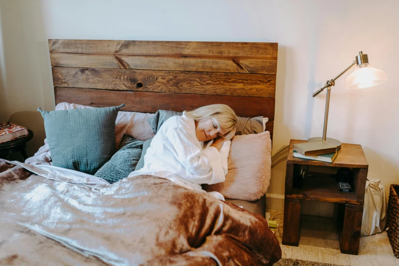 a woman laying on top of a bed covered in a blanket, by Carey Morris, pexels, wooden furniture, background image, sydney sweeney, tired half closed