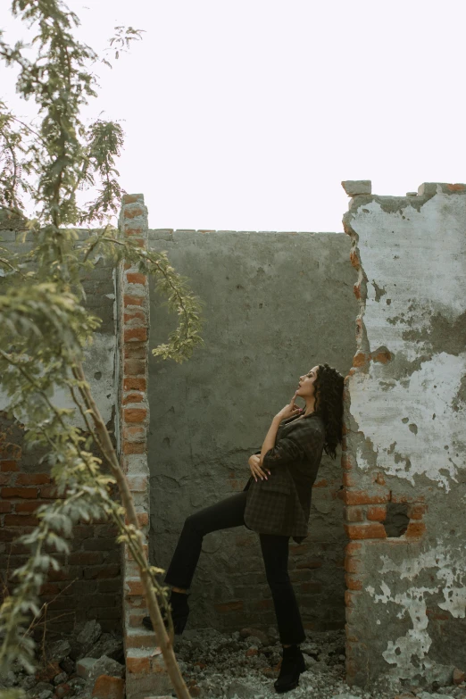 a woman standing next to a brick wall, a picture, pexels contest winner, wrecked buildings, low quality photo, with trees, full body within frame