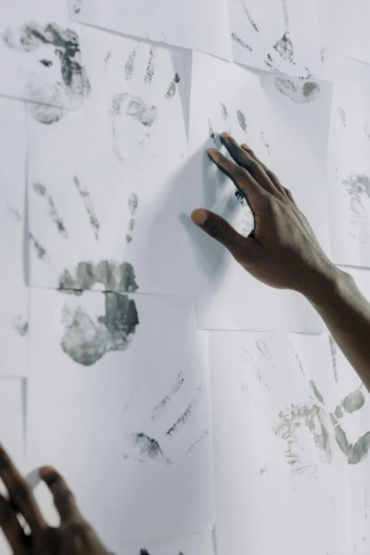 a person touching a piece of paper on a wall, by Arabella Rankin, trending on pexels, visual art, fingerprints on clay, man is with black skin, many hands, film still promotional image