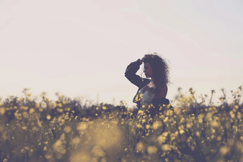 a woman standing in a field of yellow flowers, a picture, by Lucia Peka, pexels, romanticism, silhouettes in field behind, with instagram filters, looking left, low colour