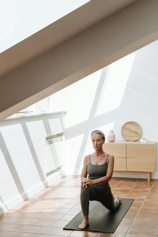 a woman sitting on a yoga mat in a room, light and space, slanted ceiling, standing near a window, amanda lilleston, terracotta