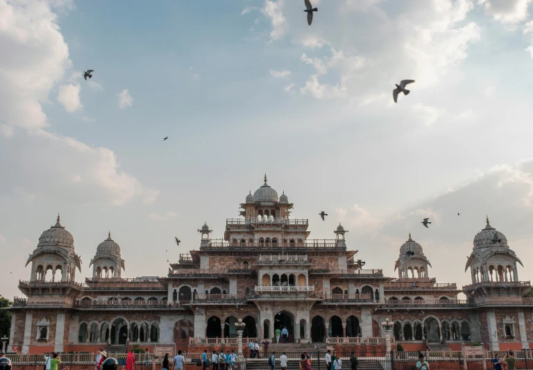 a group of people standing in front of a large building, by Julia Pishtar, pexels contest winner, india, birds flying in the distance, moorish architecture, dragons flying in the sky