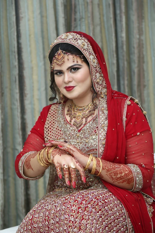 a woman in a red dress sitting on a bed, an album cover, inspired by Ambreen Butt, pixabay, qajar art, thick fancy makeup, wedding, thumbnail, hands