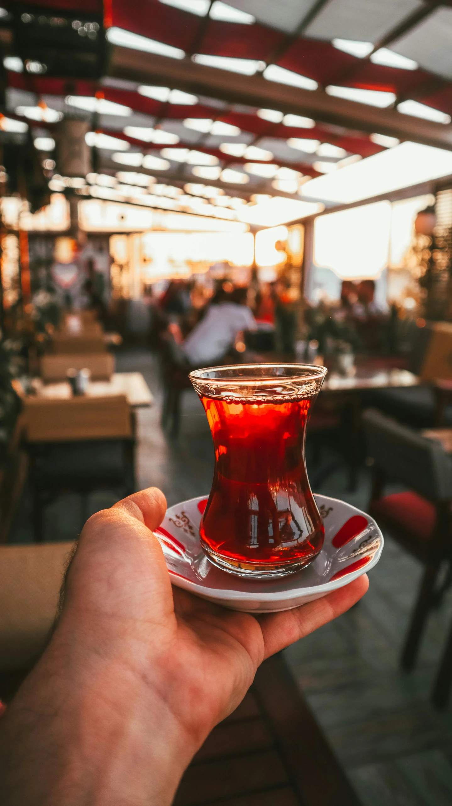 a person holding a cup of tea in a restaurant, by Niko Henrichon, pexels, hurufiyya, turkish and russian, square, paler. millions of glass-walled, maroon