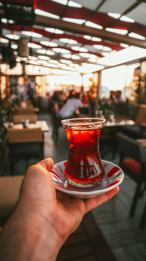 a person holding a cup of tea in a restaurant, by Niko Henrichon, pexels, hurufiyya, turkish and russian, square, paler. millions of glass-walled, maroon