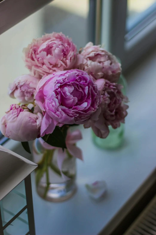 a vase filled with pink flowers sitting on a window sill, peonies, color photograph, close - up photograph, tall