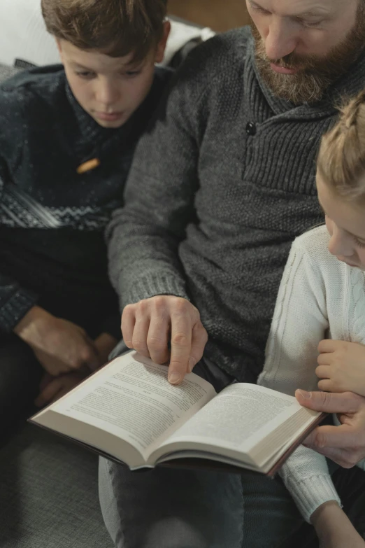 a man and two children sitting on a couch reading a book, by Jacob Toorenvliet, pexels, incoherents, praying, gif, cinematic still, school class