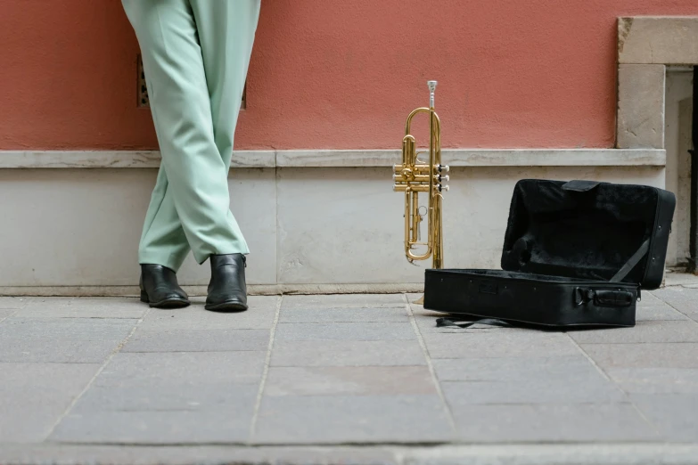 a person leaning against a wall with a trumpet, by Emma Andijewska, pexels contest winner, bags on ground, in a square, green legs, sales