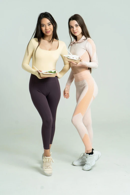 two women standing next to each other holding plates of food, an album cover, inspired by Wang Duo, trending on pexels, in spandex suit, beige, grape, cute sportswear