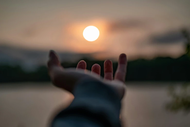 a person holding their hand out in front of the sun, dusk setting, looking straight forward, floating away, subtle detailing