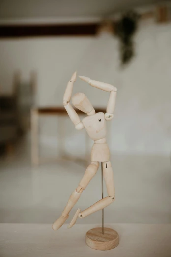 a wooden mannequin sitting on top of a table, unsplash, kinetic art, kawaii playful pose of a dancer, 1 figure only, lower quality, indoor picture