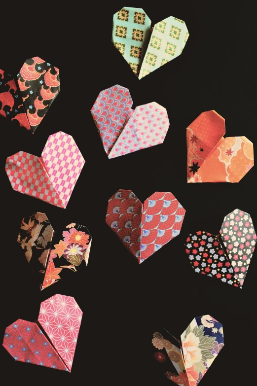 a bunch of origami hearts on a black background, by Jessie Algie, japanese collection product, in detail, puce and vermillion, made of paper