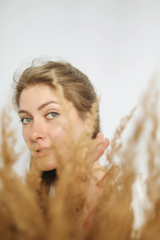 a woman standing in front of a bunch of dry grass, unsplash, renaissance, soft facial features, looking into a mirror, plain background, portrait image