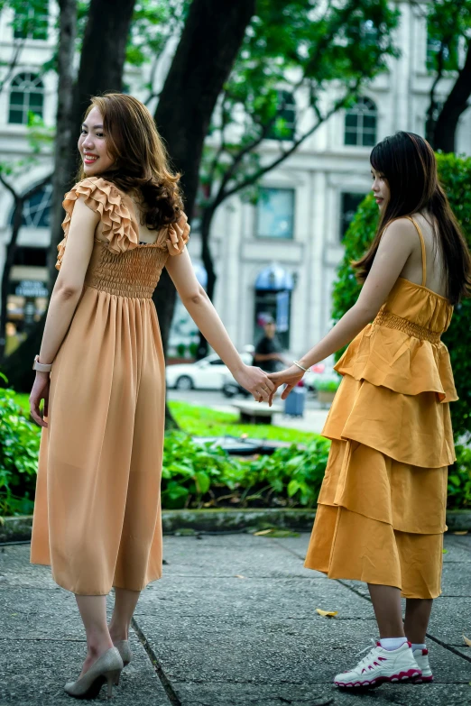 a couple of women standing next to each other holding hands, shutterstock, renaissance, vietnam, pale orange colors, woman in dress, afternoon hangout