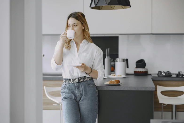 a woman drinking a cup of coffee in a kitchen, by Sebastian Vrancx, pexels contest winner, happening, wearing jeans, smart casual, eleanor tomlinson, gif