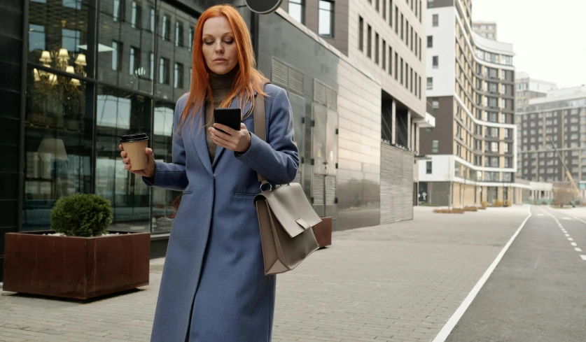 a woman in a blue coat is looking at her cell phone, trending on pexels, realism, young redhead girl in motion, walking to work, trending on unreal engine, cool marketing photo