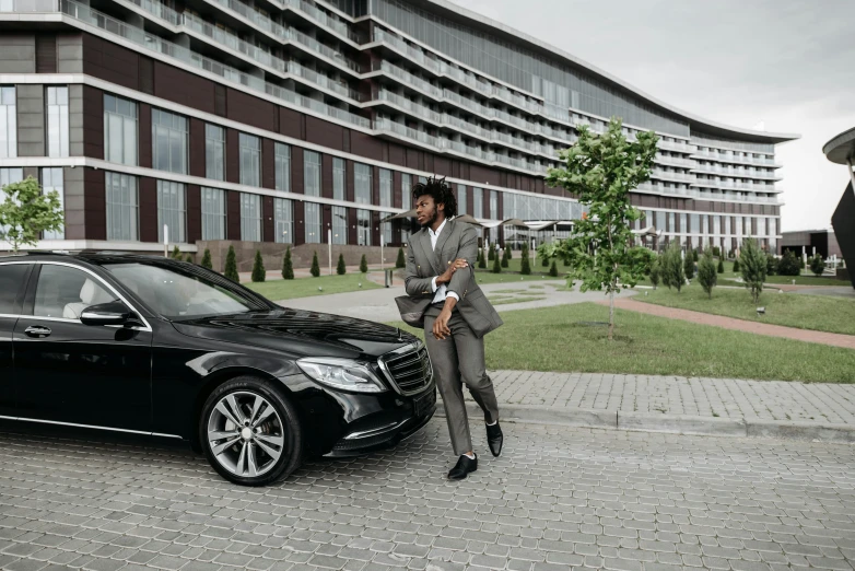 a man in a suit standing next to a black car, pexels contest winner, hurufiyya, mercedez benz, in style of kyrill kotashev, celebrating, man is with black skin