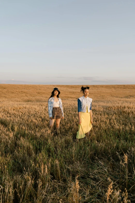 two women standing in a field of tall grass, an album cover, unsplash, lulu chen, wearing farm clothes, wide long view, badlands