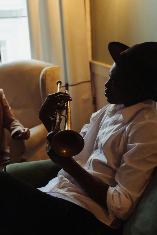 a man sitting in a chair holding a trumpet, by Arabella Rankin, pexels contest winner, lupita nyong'o, at the sitting couch, very grainy, promotional image