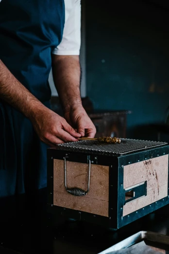a close up of a person holding a box, by Jacob Toorenvliet, pexels contest winner, renaissance, blacksmith apron, made of bees, chef table, press shot