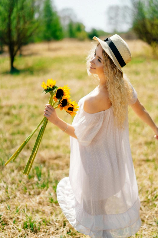 a woman holding a bunch of sunflowers in a field, unsplash, romanticism, white summer dress, with hat, a blond, walking confidently