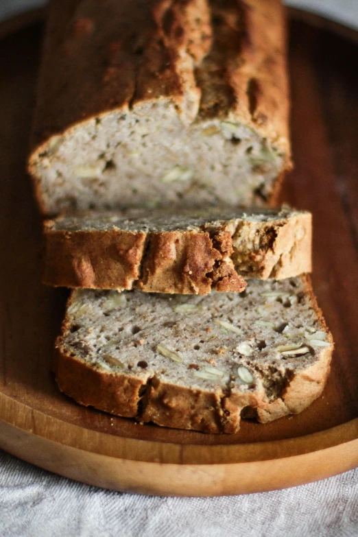 a loaf of bread sitting on top of a wooden plate, botanicals, cut, seeds, award - winning crisp details ”