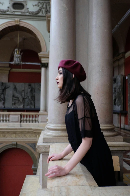 a woman standing on a ledge in a building, inspired by Jeanne Hébuterne, pexels contest winner, black beret, maroon hat, belle delphine, sheer