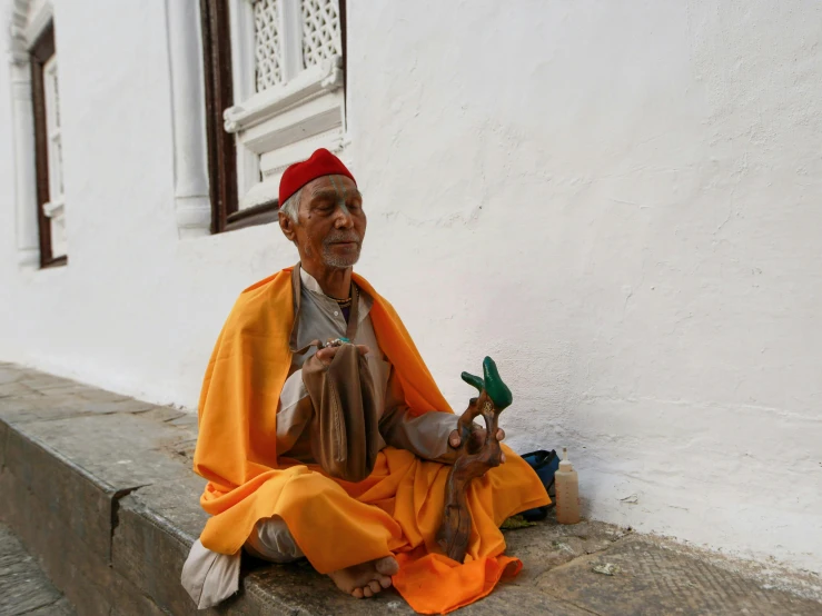 an old man sitting on the side of a building, dressed as an oracle, traditional clothes, vastayan, begging