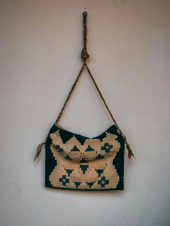 a close up of a purse hanging on a wall, a cross stitch, by Jessie Algie, unsplash, folk art, brutalist aztec architecture, 2 5 6 x 2 5 6 pixels, navy, grainy vintage