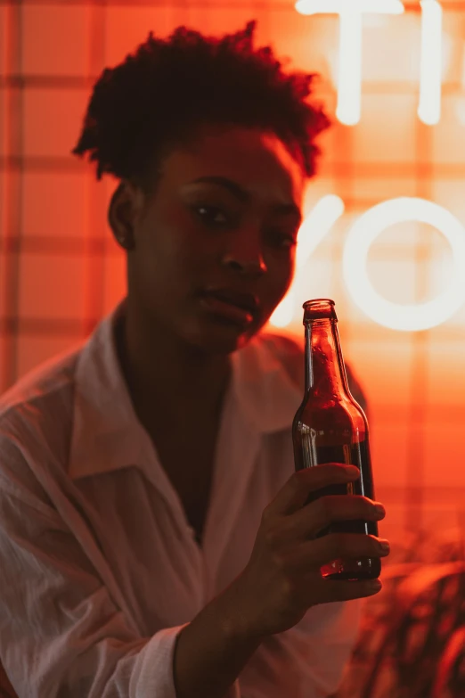 a woman holding a beer bottle in front of a neon sign, a stock photo, by Cosmo Alexander, pexels contest winner, renaissance, black teenage boy, androgynous person, red and orange glow, on a pale background