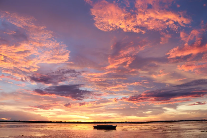 a boat sitting on top of a body of water, by Peter Churcher, pexels contest winner, romanticism, panorama view of the sky, orange / pink sky, liquid gold, big island