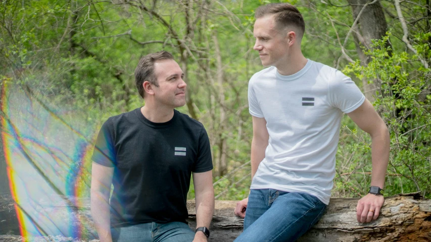 two men sitting on a log in the woods, a portrait, pexels contest winner, symbolism, wearing a black t-shirt, lgbt, official store photo, white and black clothing