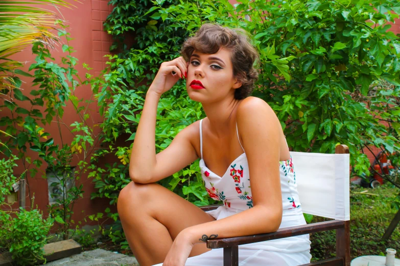 a woman sitting on top of a wooden bench, a portrait, inspired by Elsa Bleda, pexels contest winner, art nouveau, pinup model, wearing white camisole, curly pixie cut hair, red lips