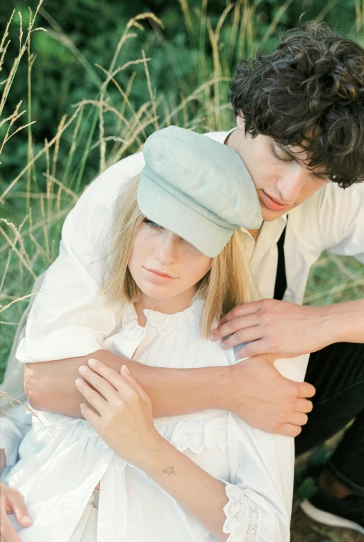 a couple of people that are sitting in the grass, a colorized photo, by Elsa Bleda, pexels, renaissance, breton cap, white and pale blue, holding close, heartbreak