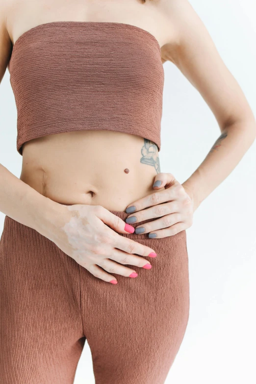 a woman with a tattoo on her stomach, trending on pexels, on a pale background, belly button showing, brown, colorized