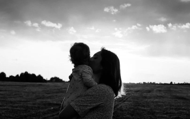 a woman holding a baby in a field, a black and white photo, unsplash, sunlit sky, kissing, 1 6 x 1 6, 15081959 21121991 01012000 4k