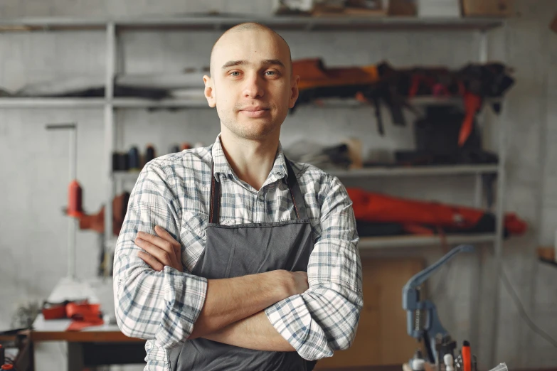 a man standing in a workshop with his arms crossed, a portrait, inspired by Jakub Husnik, pexels contest winner, avatar image, leather apron, portrait of bald, professional profile picture