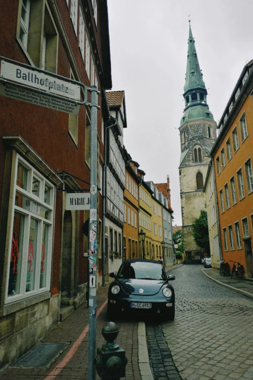 a car is parked on a cobblestone street, an album cover, hannover, church in the background, taken with kodak portra, square