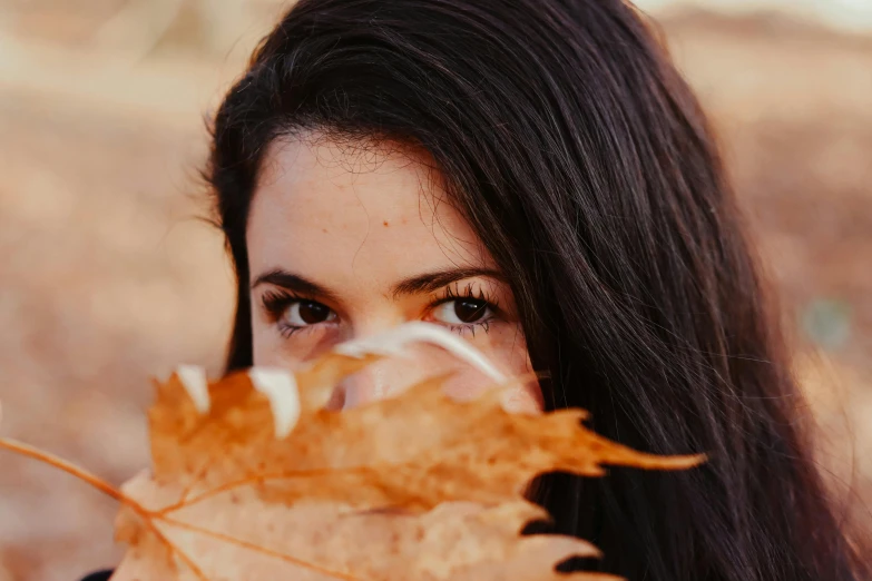 a woman holding a leaf in front of her face, pexels contest winner, hurufiyya, girl with dark brown hair, profile image, brown hair and large eyes, 🍂 cute