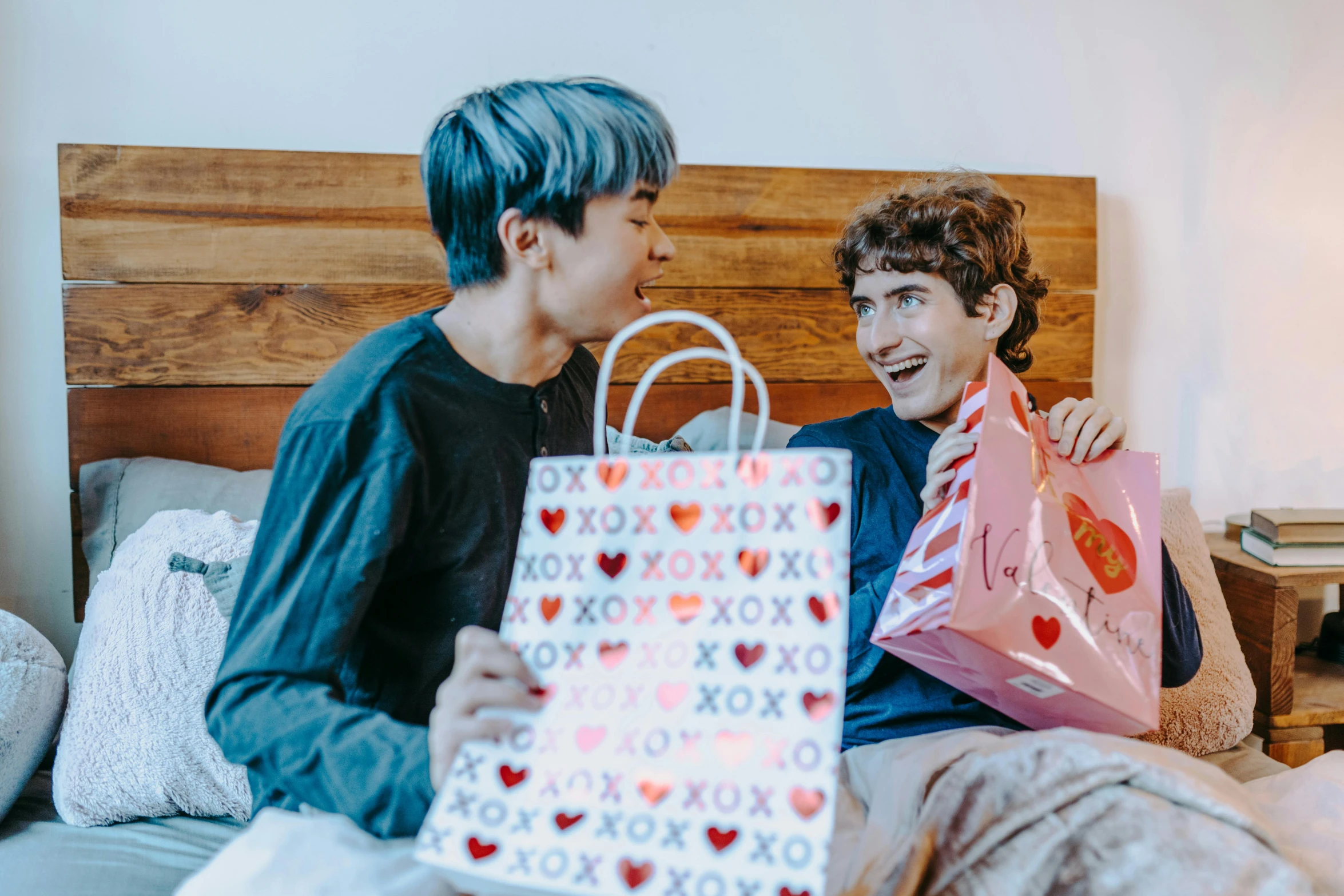 a couple of young men sitting on top of a bed, by Julia Pishtar, pexels contest winner, holding gift, kawaii vibe, smiling at each other, people shopping