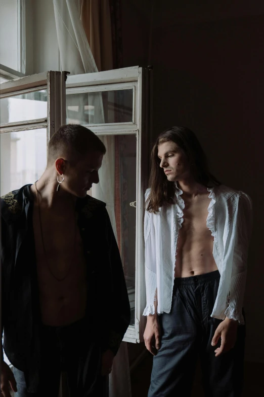 a man and a woman standing in front of a window, an album cover, by Attila Meszlenyi, unsplash, renaissance, androgynous male, cute boys, disrobed, southern slav features