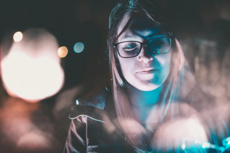 a woman in glasses looking at a cell phone, a picture, inspired by Elsa Bleda, pexels contest winner, lights in the night, oversaturated lens flair, looking up at camera, avatar image