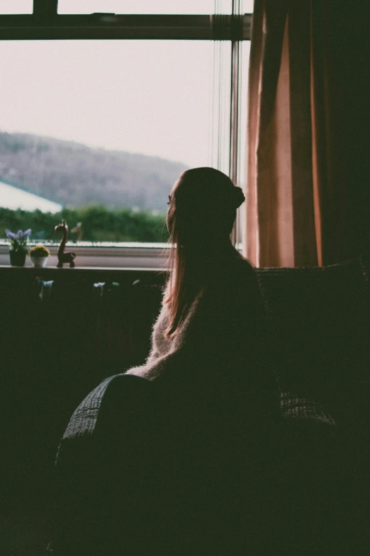 a woman sitting on a couch looking out a window, a picture, inspired by Elsa Bleda, trending on pexels, portrait of depressed teen, facing away, low quality photo, instagram post