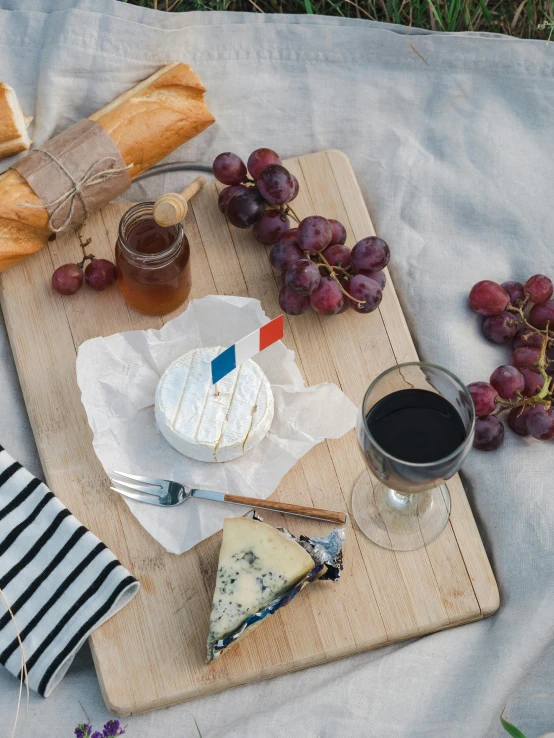 a wooden cutting board topped with cheese and grapes, pexels contest winner, in paris, picnic, dark blue and white robes, drink