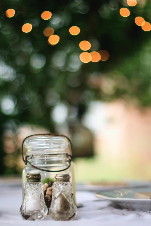 a glass jar sitting on top of a table, a picture, by Jessie Algie, unsplash, light and space, lanterns, garden setting, 4 5 mm bokeh, low iso