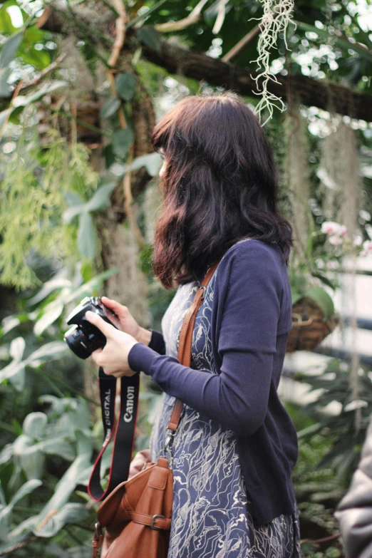 a woman standing in a garden holding a camera, a picture, by Basuki Abdullah, botanic garden, indoor picture, over the shoulder, professional photo-n 3