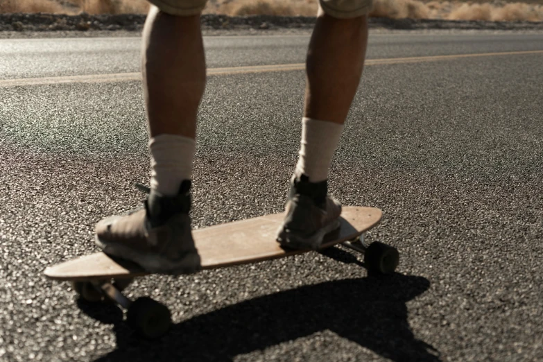 a man riding a skateboard down the middle of a road, a picture, unsplash, photorealism, large thighs, faded and dusty, alana fletcher, gum rubber outsole