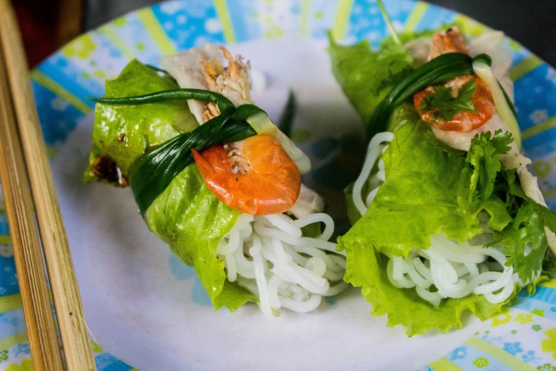 a close up of a plate of food with chopsticks, wrapped arms, lettuce, basil gogos, frill